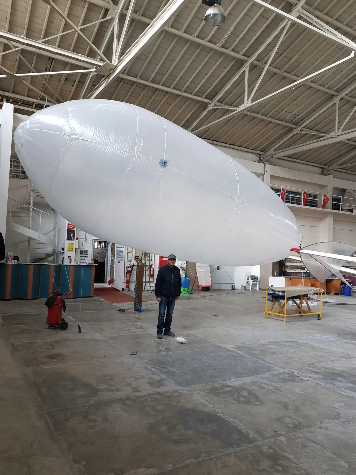 Photograph of the Eskişehir sub-scale demonstrator suspended in a hangar, with a person beneath it